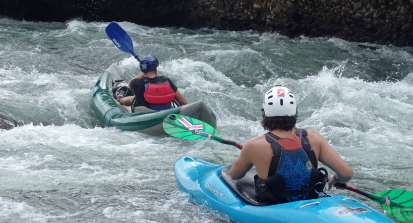 Two people wearing safety gear paddle two watercraft through whitewater 